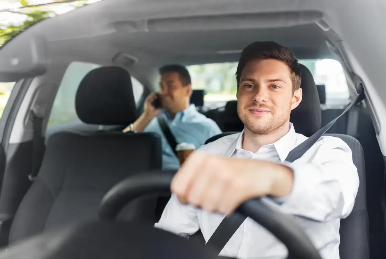 Driver wearing a fastened three-point seat belt at the wheel of a vehicle with a passenger behind