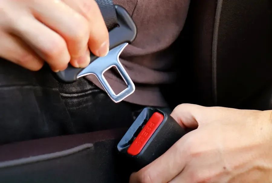 Hands engaging a seat belt latch plate into its buckle receiver during a fitment check